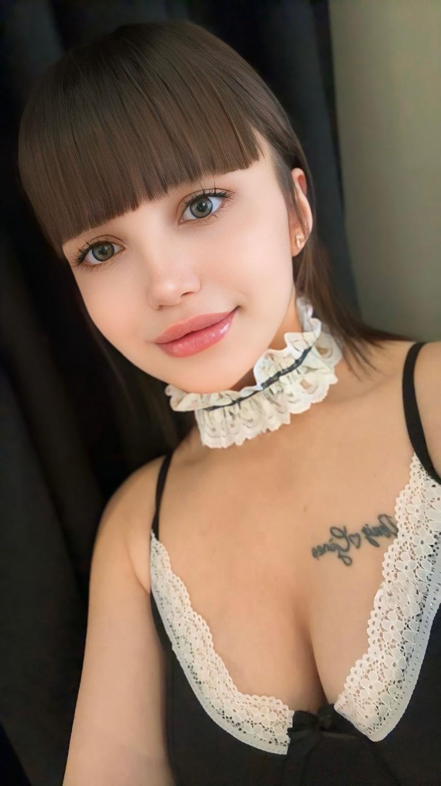 Close-up portrait of a woman with straight brown bangs, wearing a white lace choker and black lace-trim top.