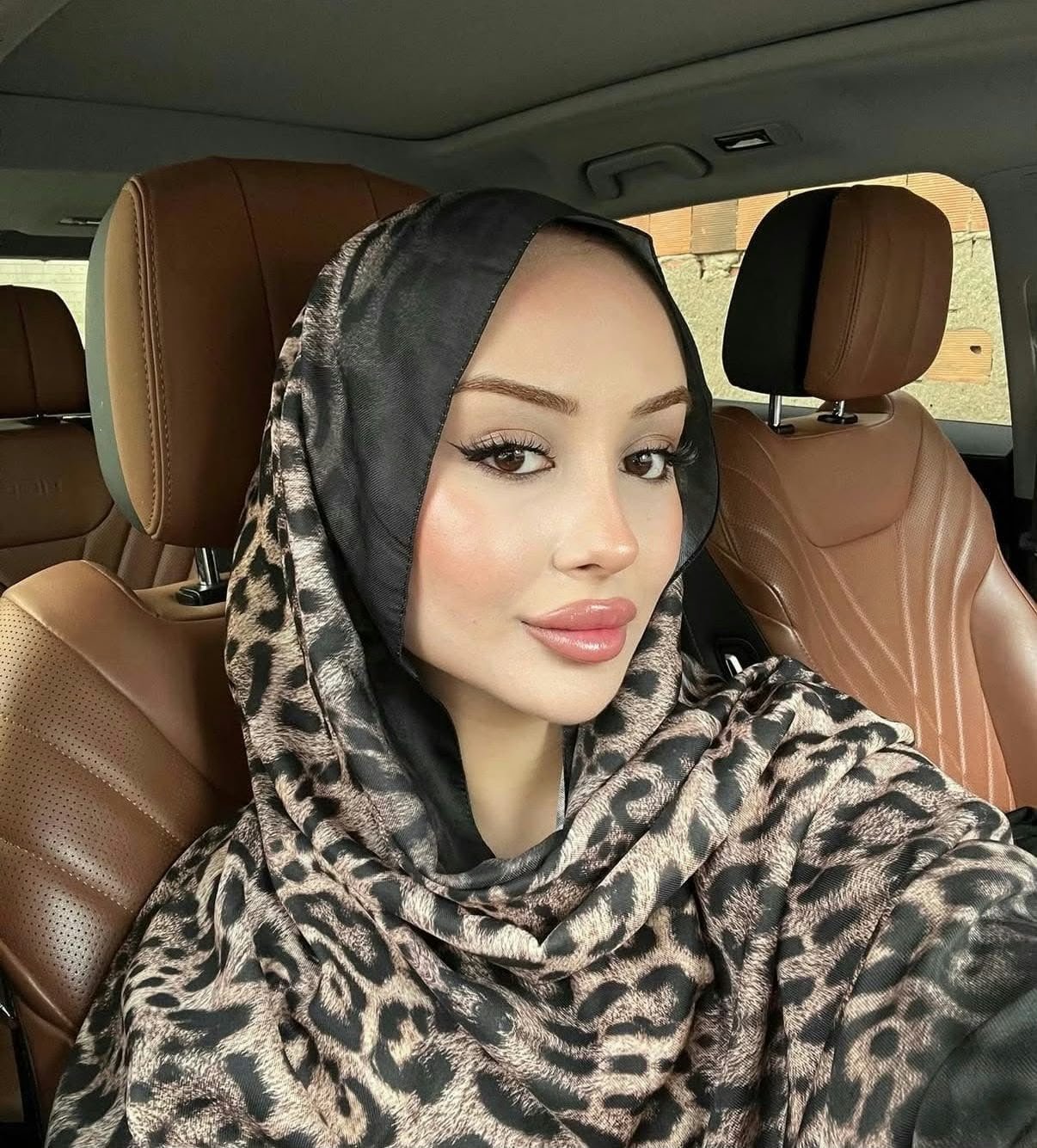Close-up of a woman wearing a leopard-print hijab in a car with tan leather seats behind her.