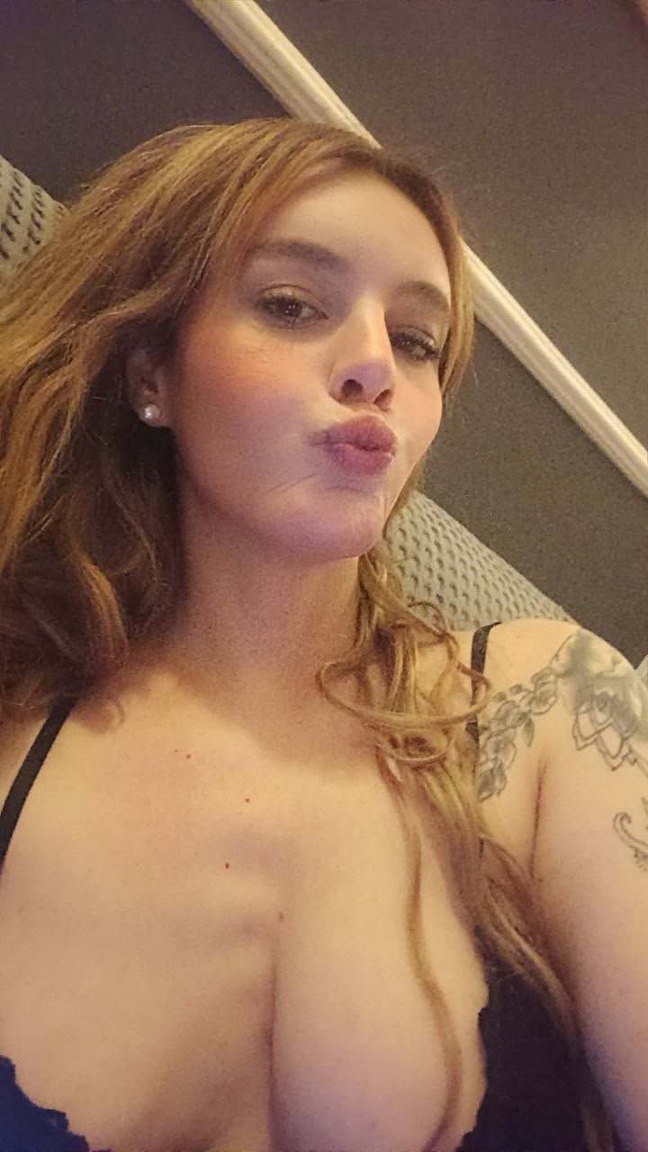 Woman with light brown hair puckering lips for a selfie, wearing a black top, with a visible tattoo on the right arm.