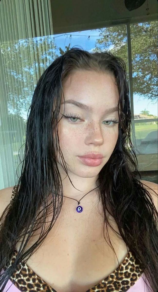 Woman with wet hair and light makeup, wearing a leopard-print top and blue evil-eye necklace outdoors.